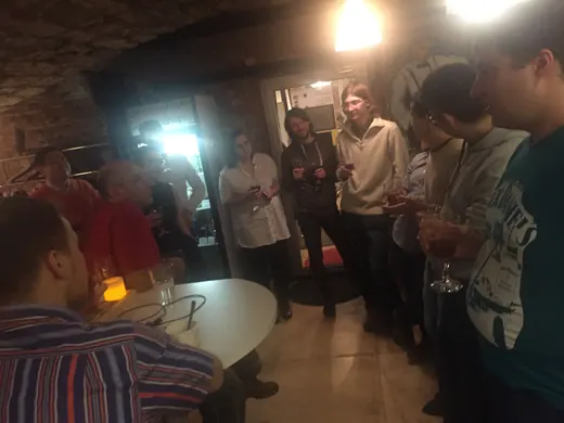 A crowd standing with drinks, the lights bright behind them