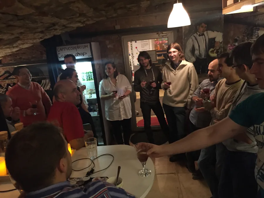 A room full of people with glasses, an arm reaching in with a drink