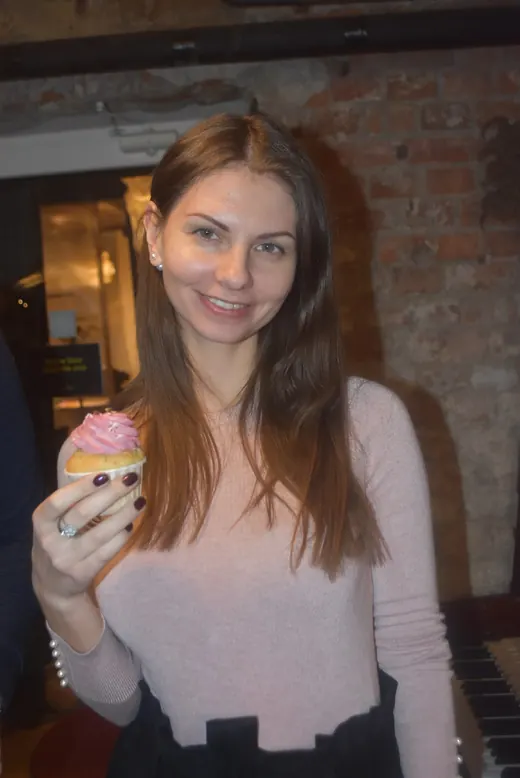 A woman smiling, holding a cupcake