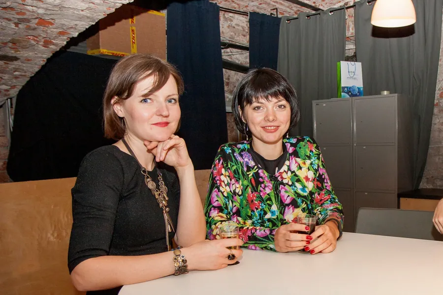 Two women at a table, one with her chin on her hand, smiling