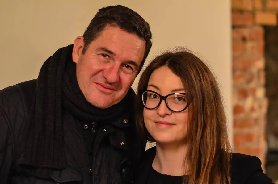 A man in a scarf and a woman in glasses, cheek to cheek, smiling