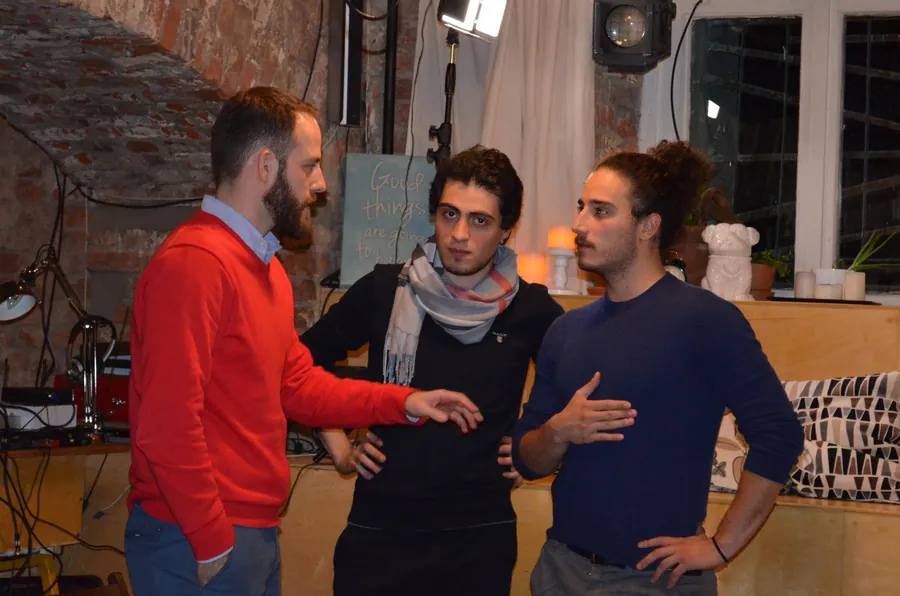 A man in a red jumper listening to a man with a scarf