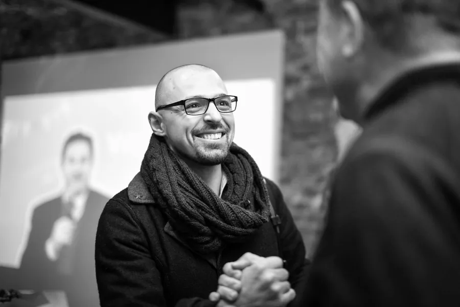 A man in glasses laughing, hands clasped, in black and white