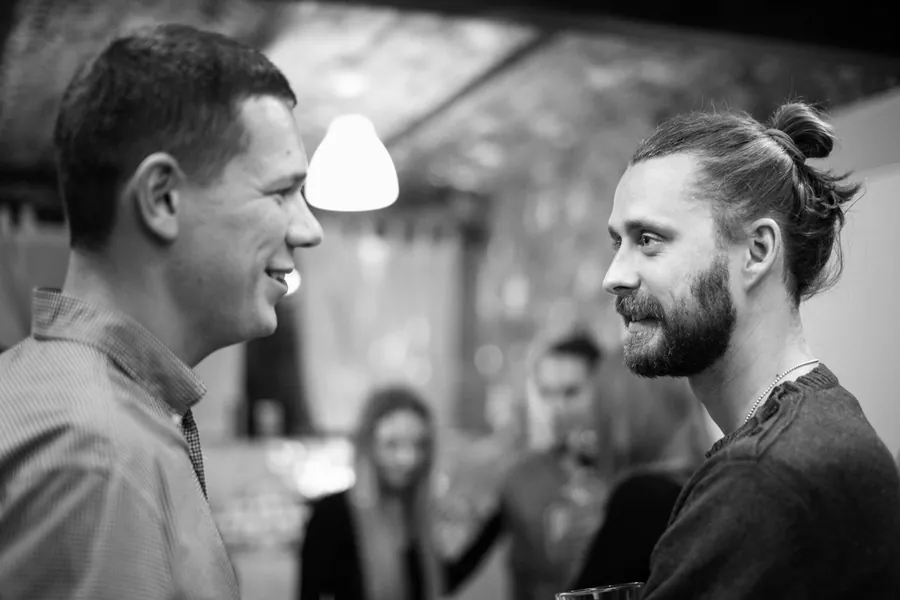 Two men talking under a pendant lamp, in black and white