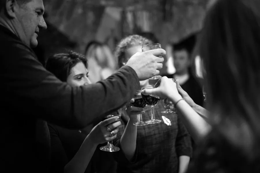 Glasses raised in a toast across a crowded room, in black and white