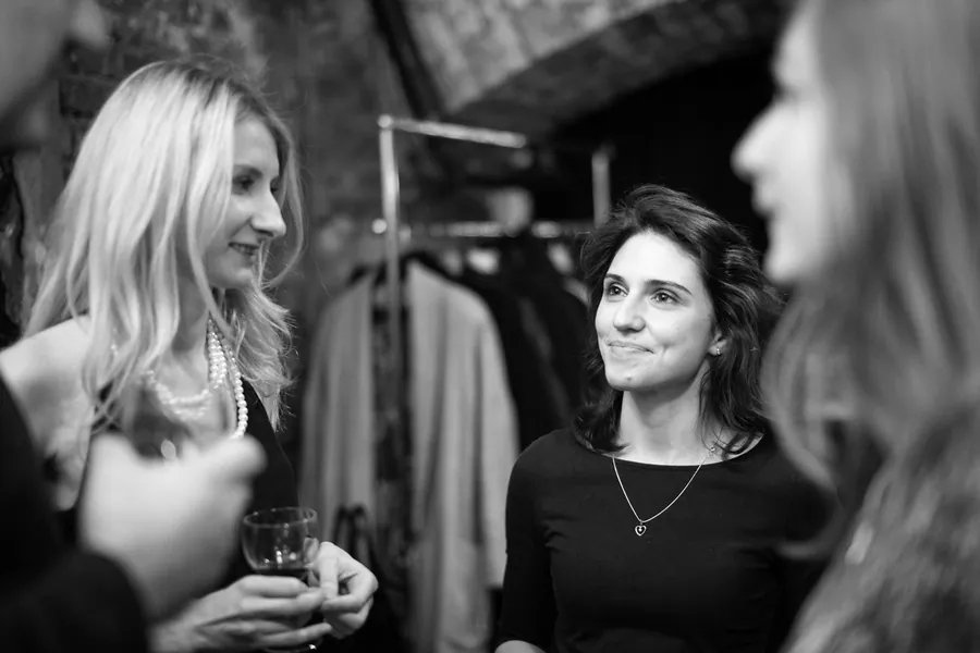 Two women talking, one with a glass of wine, in black and white