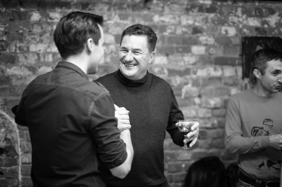 Two men laughing, one mid-story, in black and white