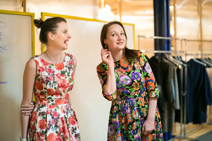 Two women in floral dresses laughing together by a doorway
