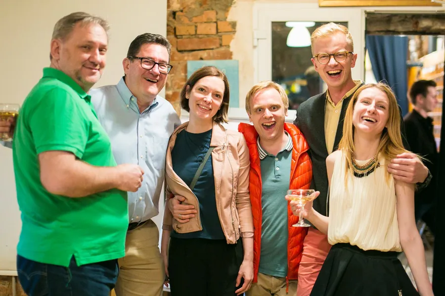 Six friends arm in arm, laughing, under the brick arches
