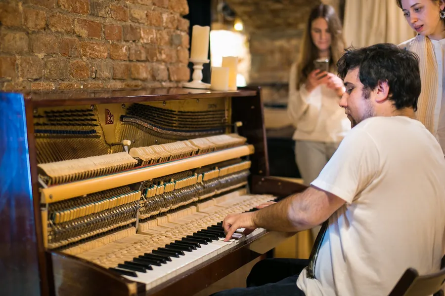 A man playing the upright piano while guests talk behind him