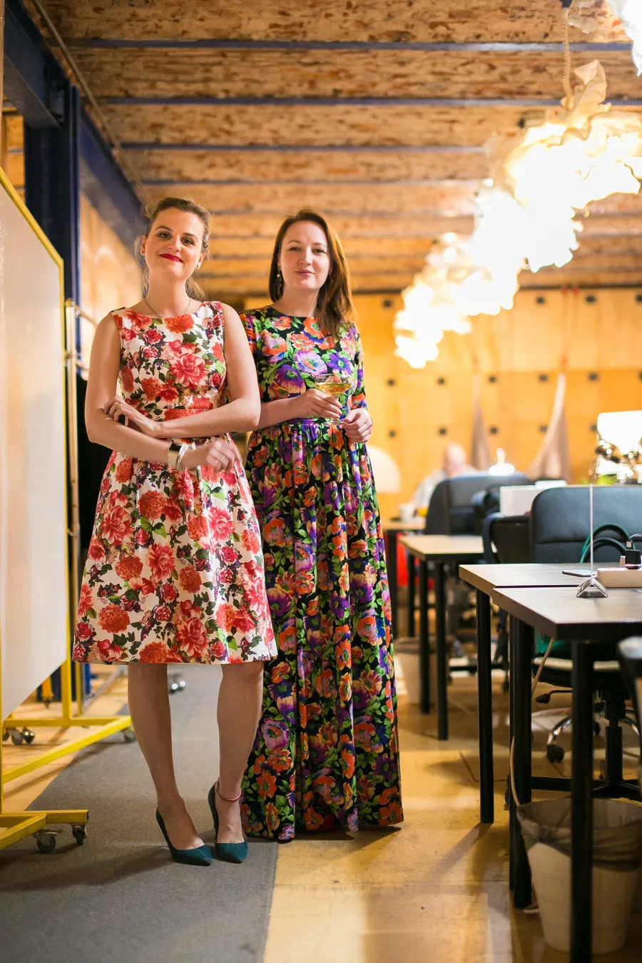 Two women in long dresses posing by the tables