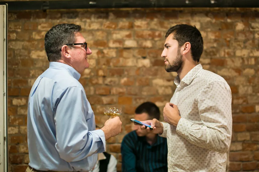 Two men talking, one in a light blue shirt with a glass