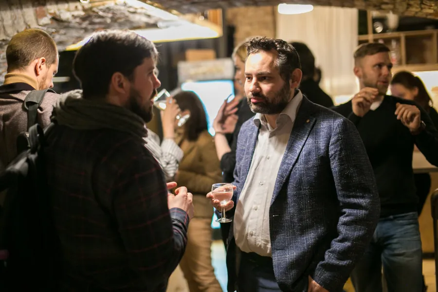 Two men talking, one in a blue blazer with a glass