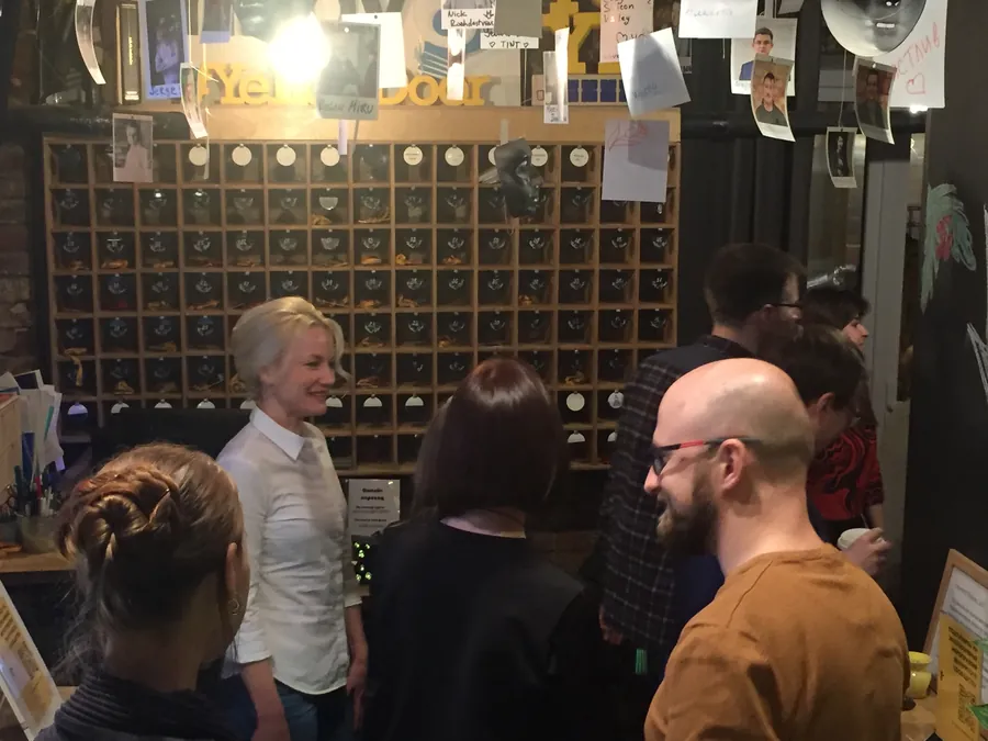 People talking by the wine rack, a woman in white